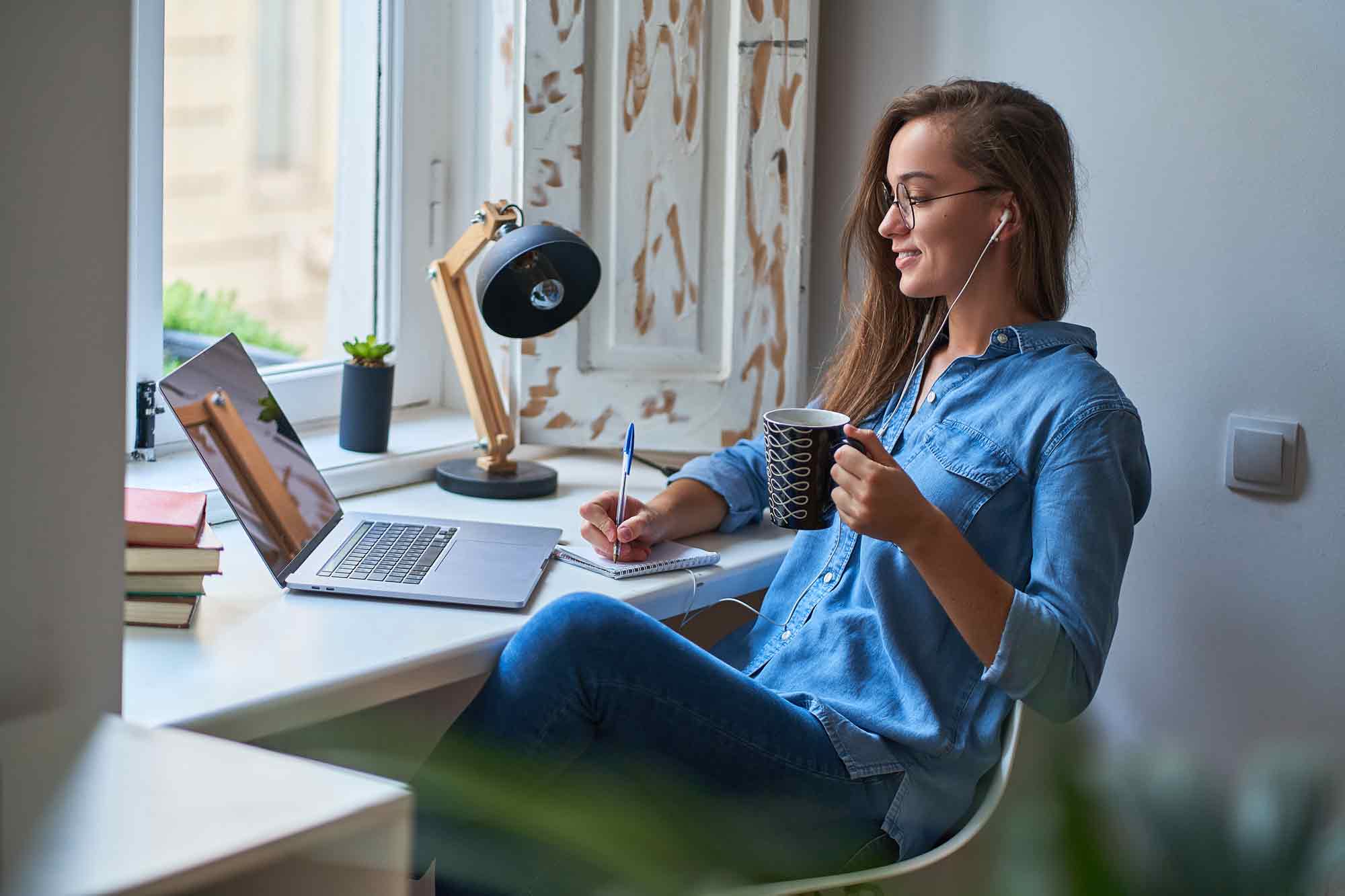 casual-young-smiling-smart-woman-student-headphones-satisfied-with-learning-foreign-language-female-making-notes-notebook-watching-webinar-video-courses-online-eduation