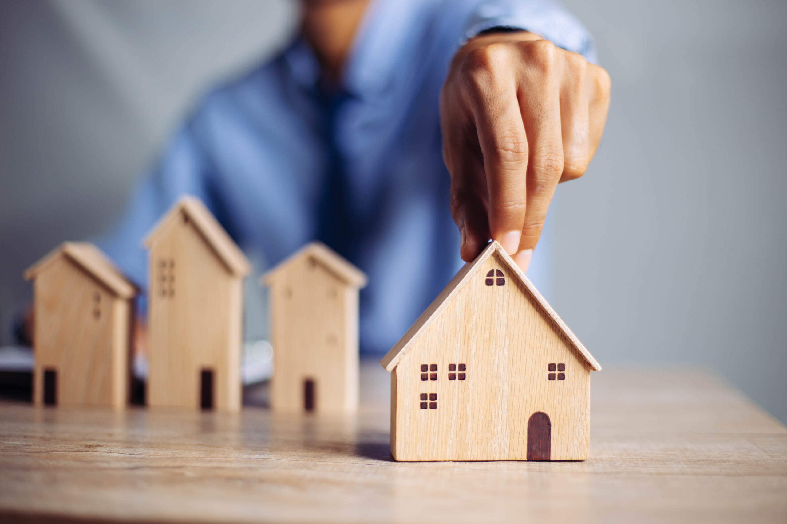 Businessman choosing mini wood house model from model on wood table, Planning to buy property. concept of Choose the best.